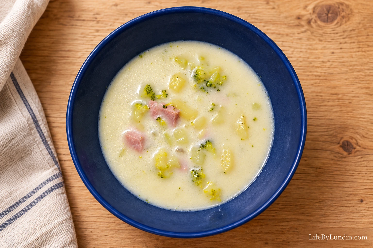 Krämig kassler- och broccolisoppa med potatistärningar i en djup blå tallrik på ett ljust träbord